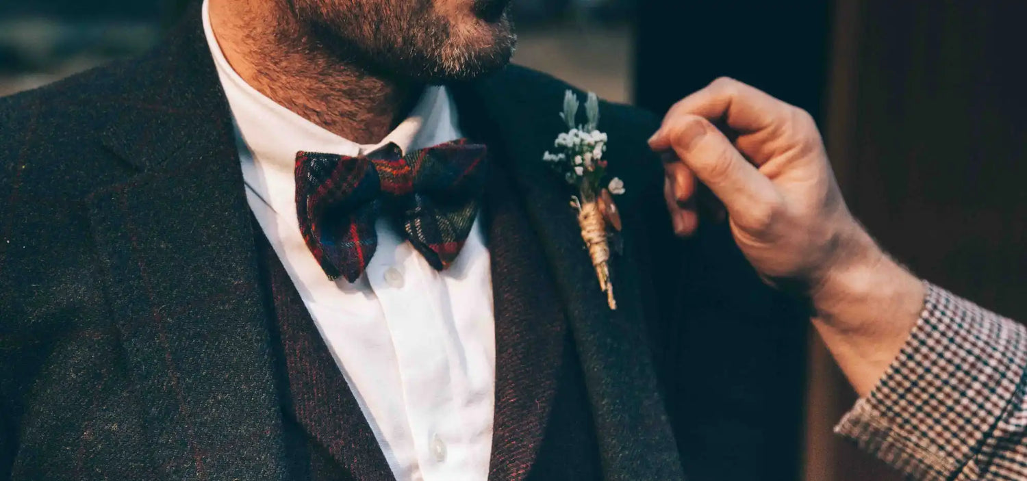 A burgundy bow tie with a floral boutonnière being adjusted.