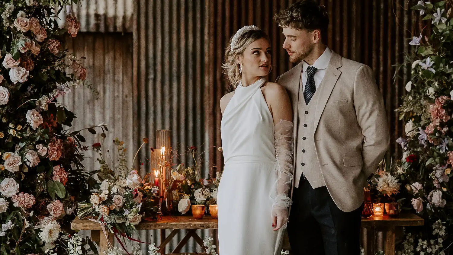 Romantic wedding couple posing amid pink floral arrangements and candlelight.